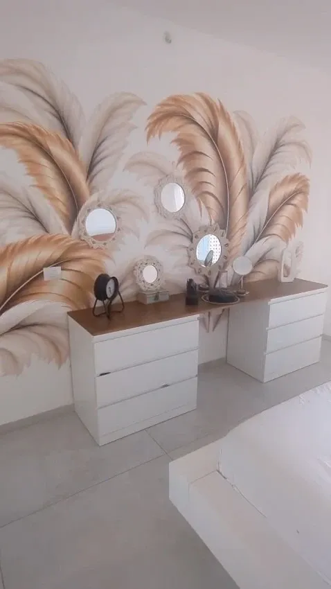 La même chambre après impression murale : grandes plumes dorées et grises sur toute la largeur