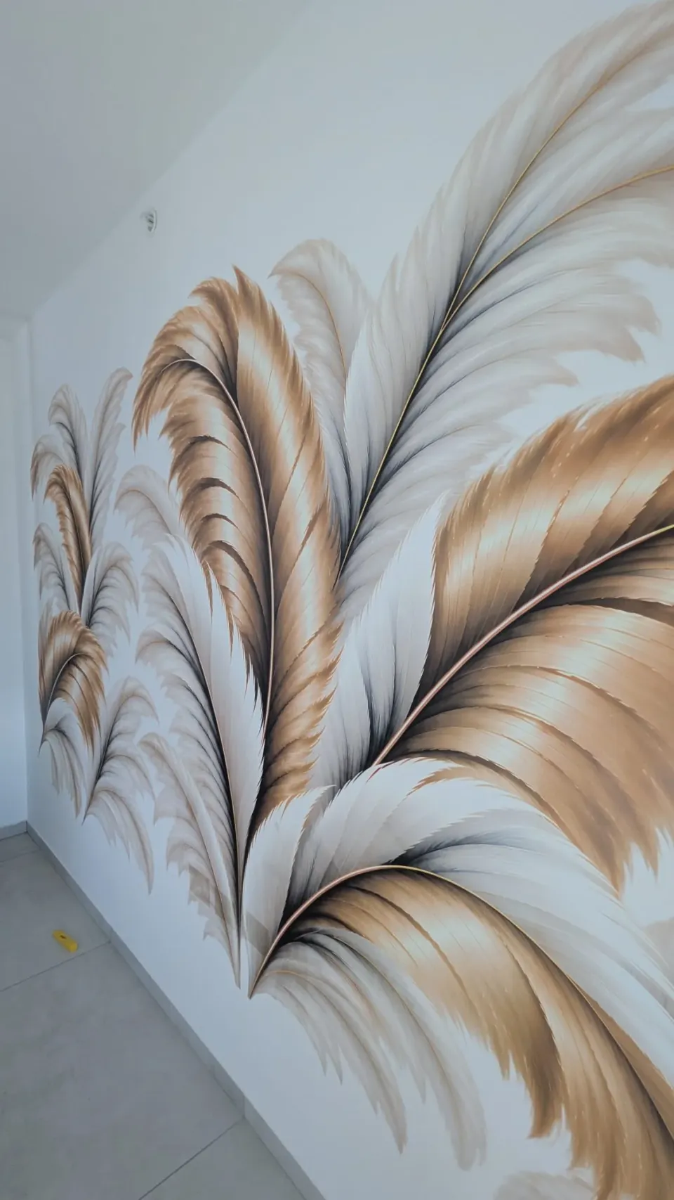 Détail d’une impression UV de plumes dorées et grises sur mur blanc